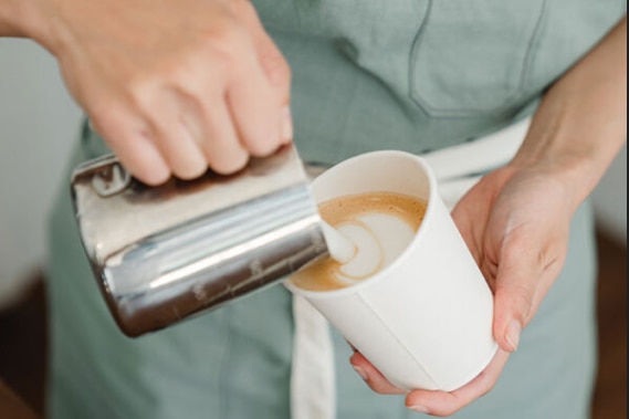 Womans hands pouring coffee from silver jug into white take away coffee cup