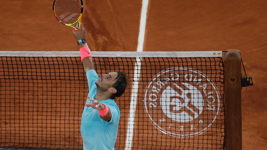 A tennis player looks to the skies, holding his arms out in triumph as he stands by the net.