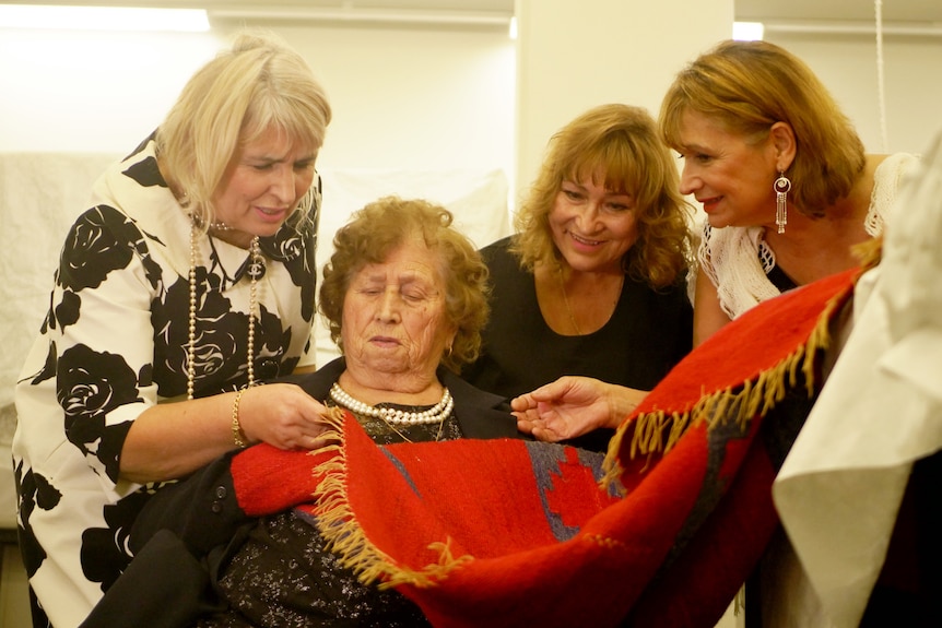 Τέσσερις γυναίκες μαζεύτηκαν γύρω από την κόκκινη υφαντή κουβέρτα