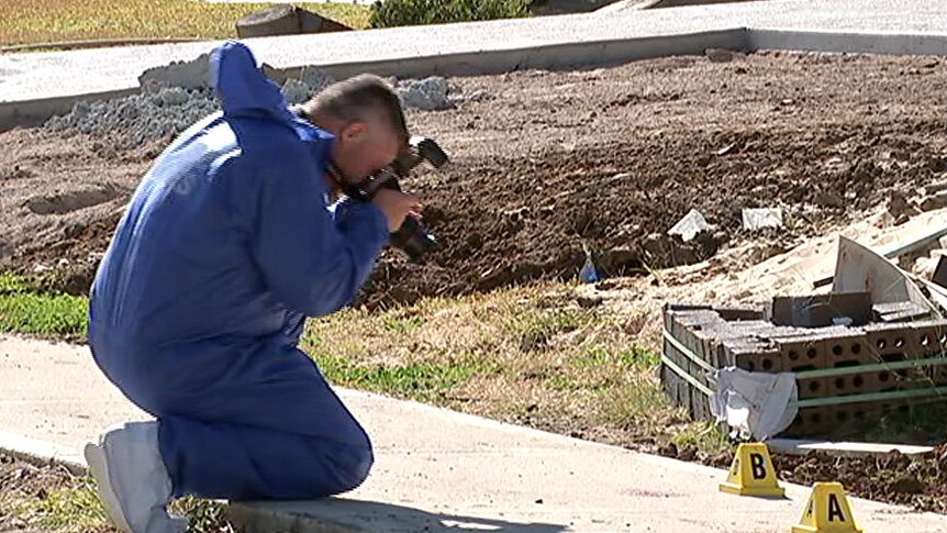 A man in blue taking photos of blood stains on a footpath.