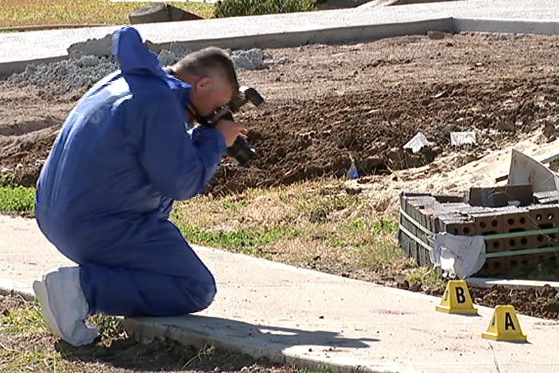 A man in blue taking photos of blood stains on a footpath.