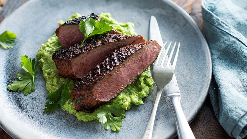 Three slices of lamb atop a avocado pea crush on a plate.