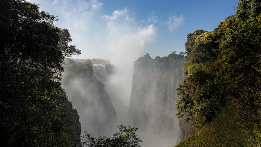A wide shot of steep cliffs in a national park with a large waterfall and a lot of mist in the distance.