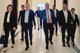 The six politicians and two other men walk through a hallway.