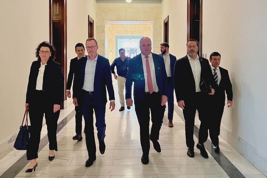 The six politicians and two other men walk through a hallway.