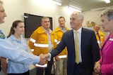A smiling Malcolm Turnbull shakes the hand of an emergency services worker as others look on.