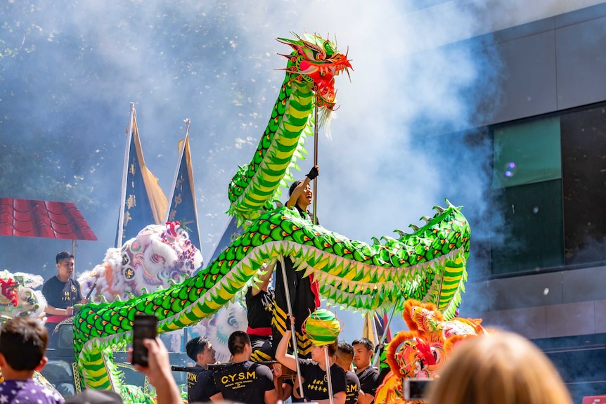 Young people perform a dragon dance as smoke from fire crackers rises in the background.