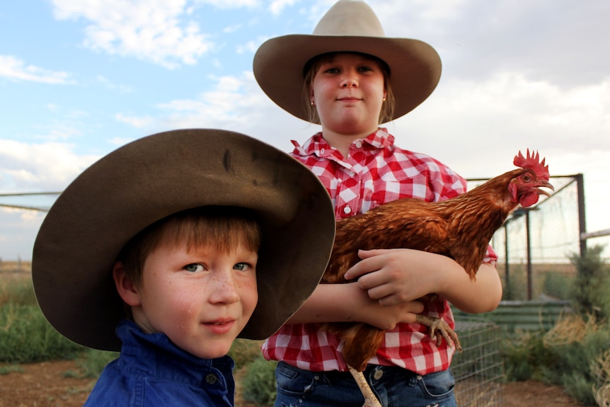 Two children wearing big hats, one holding a chicken.