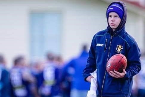 Mitchell Harwood holds a football with his right hand before an Australian rules match.