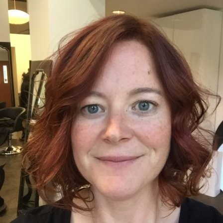 Uma mulher com cabelos ruivos cacheados sorri para a câmera.