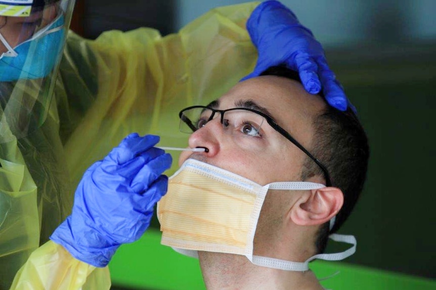 man in mask having his nostrils swabbed with a cotton stick