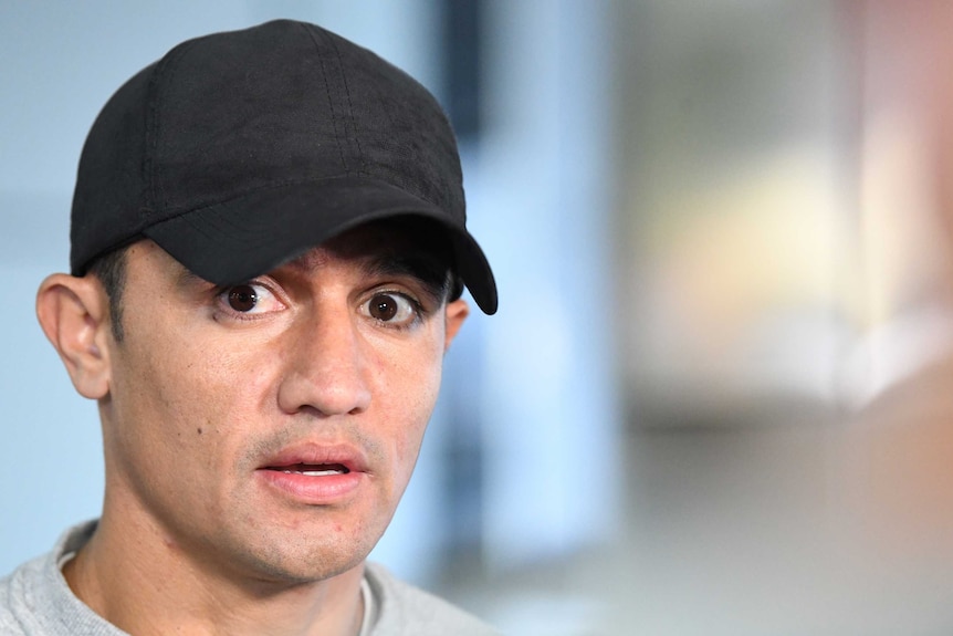 Tim Cahill wearing a cap as he speaks to the media at Melbourne Airport.