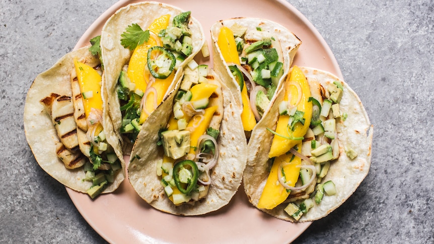 A plate of vegetarian tacos with mango, haloumi, cucumber and avocado. An easy summer dinner recipe.