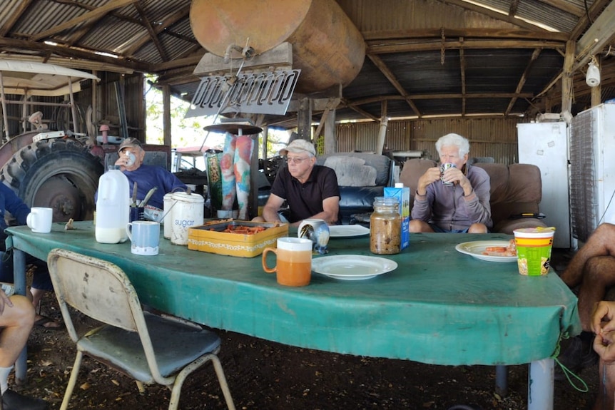 Farmers sit around a table in a farm shed. 