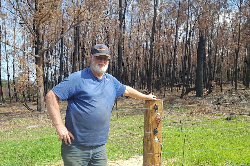 Ross Walker stands, leaning on a fence, some burnt trees behind him.