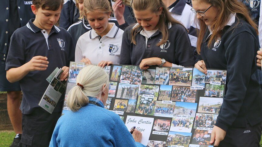 Four school children show a photo board to Dr Jane Goodall, who signs it for them.
