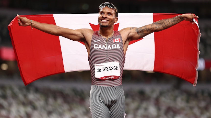 A male sprinter holds the Canadian flag behind his back after winning gold at the Tokyo Olympics.