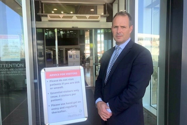 A man in a suit stands at the front of a hospital.