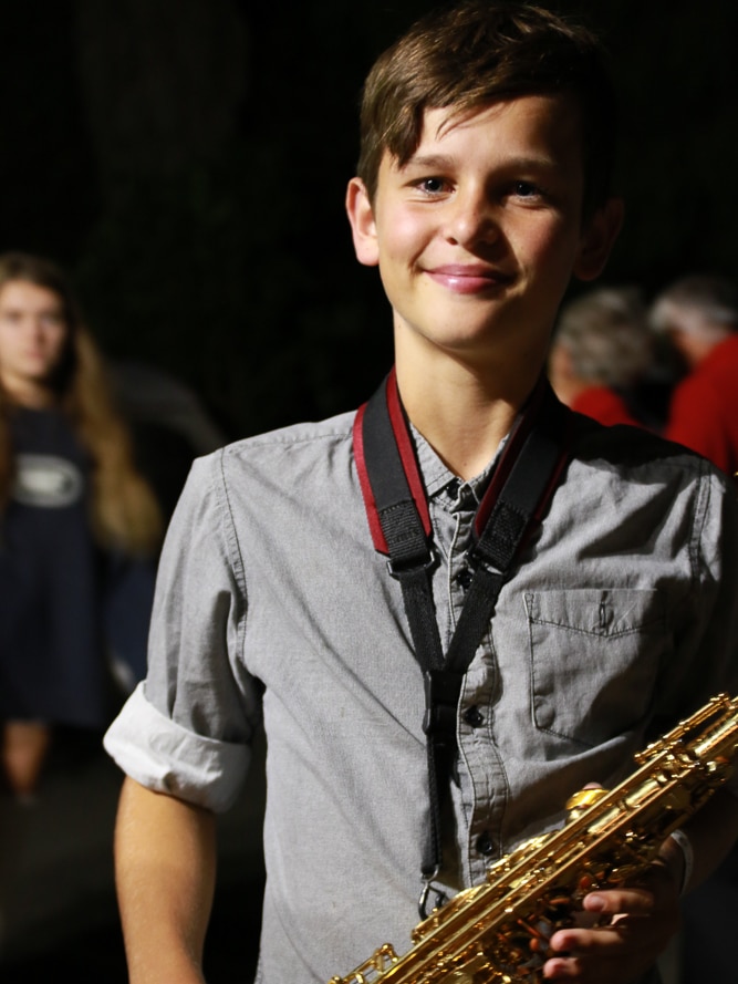 A teenage boy stands smiling with a saxophone in hand