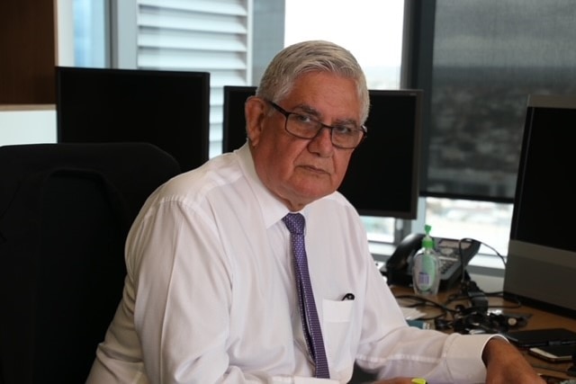 Ken Wyatt sits at a desk in an office, wearing a white shirt and purple tie, looking at the camera.