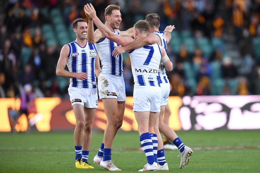 A group of North Melbourne players gather and wrap their arms around each other after a win. 
