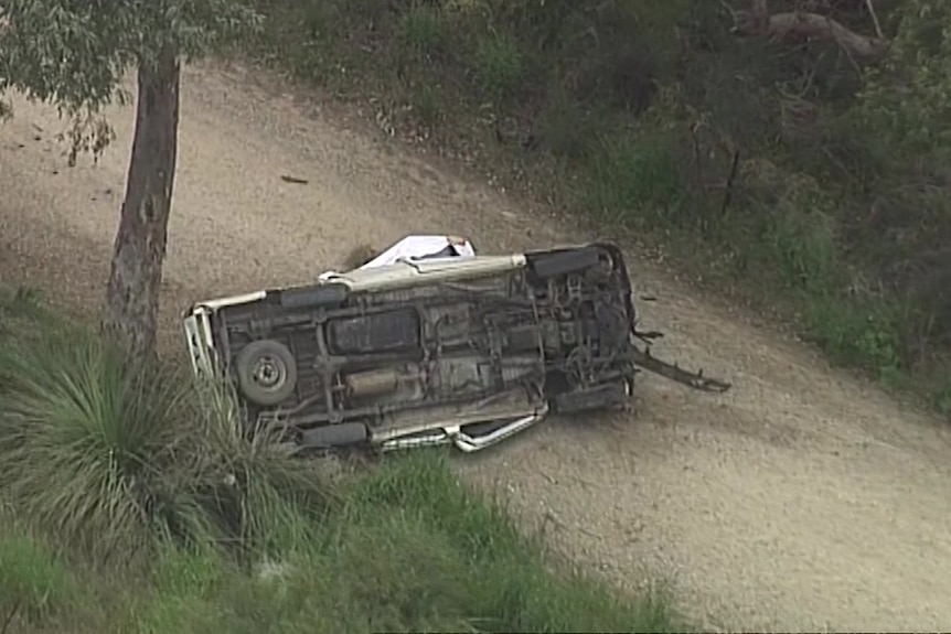 A car rollover on its roof on a dirt road among trees
