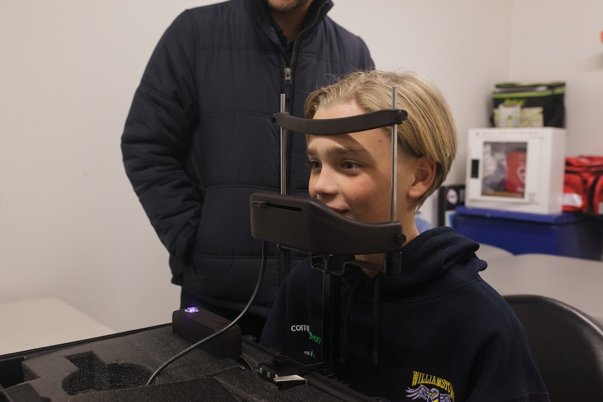 A boy sits at a device, which is scanning his eyes.