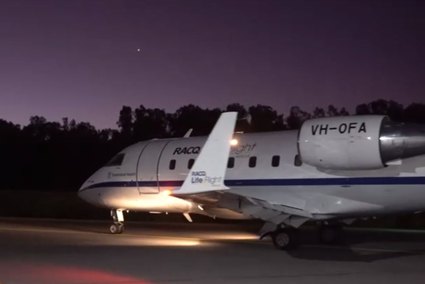 A RACQ LifeFlight Rescue Air Ambulance jet taxies along a runway at night.