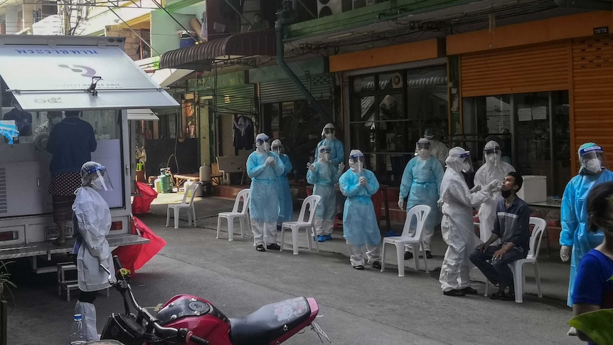 People in full PPE stand in a street while a man sitting in a plastic chair gets tested for coronavirus.