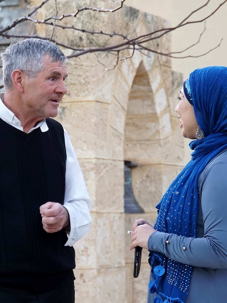 Reverend Humphries speaks with Aisha, who wears a vibrant blue hijab, in front of the church.
