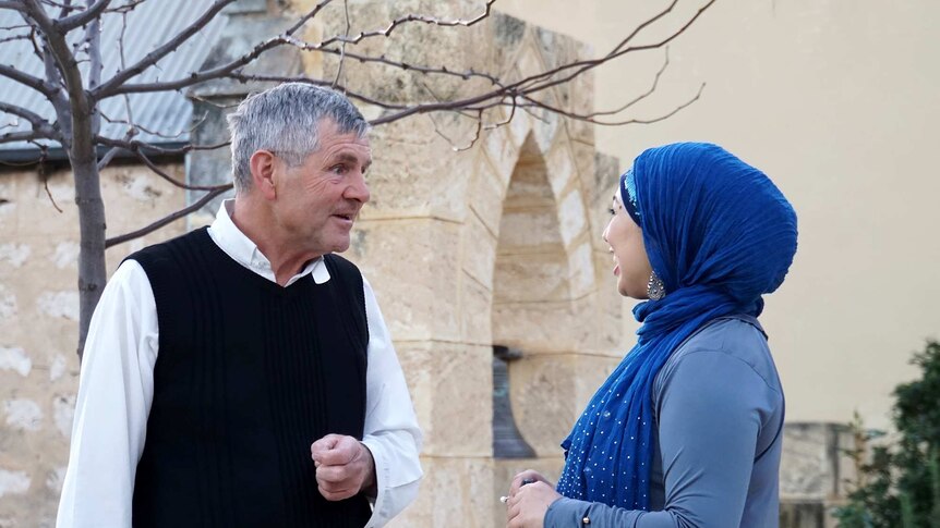 Reverend Humphries speaks with Aisha, who wears a vibrant blue hijab, in front of the church.