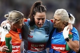 A NSW player is taken from the field by two trainers during the first Women's State of Origin match.