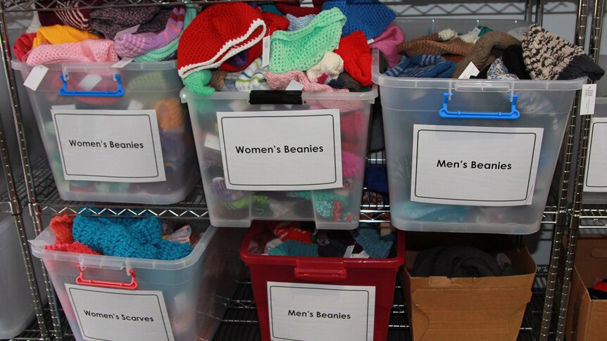 Plastic tubs filled with donated knitted goods. Each tub is labelled either women's beanies, women's scarves or men's beanies.