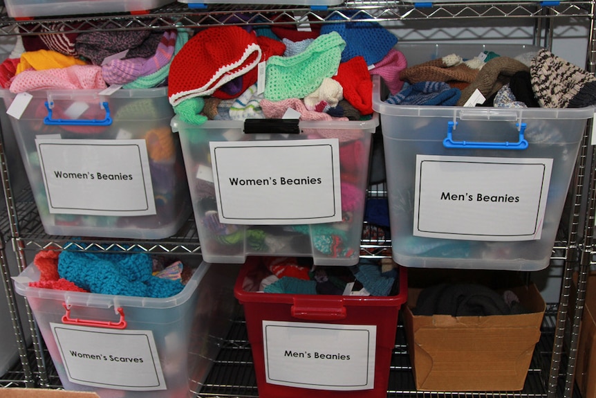 Plastic tubs filled with donated knitted goods. Each tub is labelled either women's beanies, women's scarves or men's beanies.