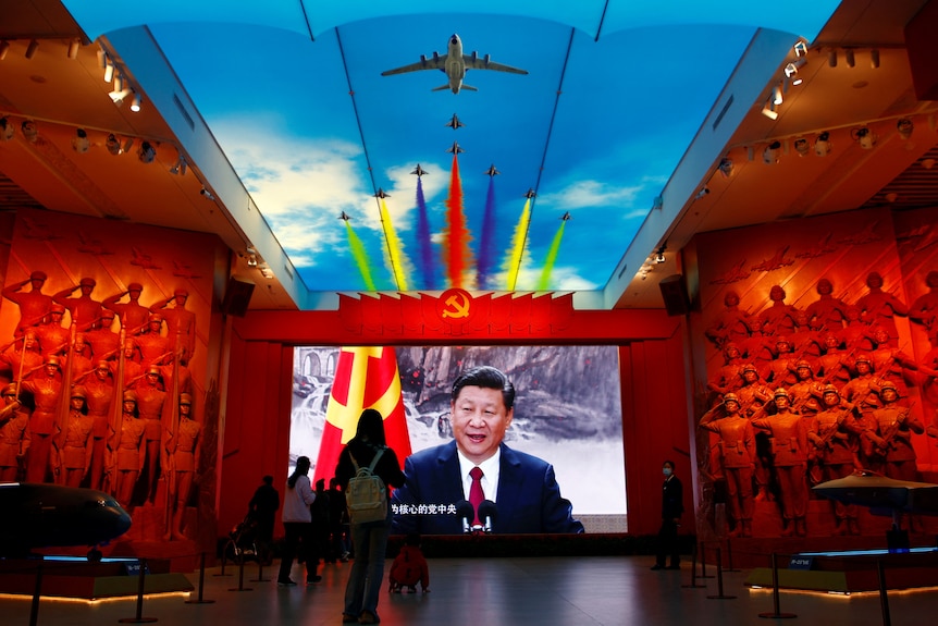 Image of dark-haired man on screen with graphic of warplanes flying above in museum