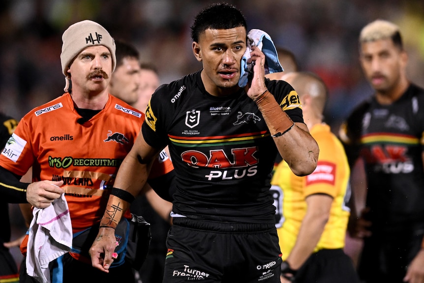 Un jugador de Penrith NRL se pone una toalla en la oreja después de ser golpeado en un placaje alto.