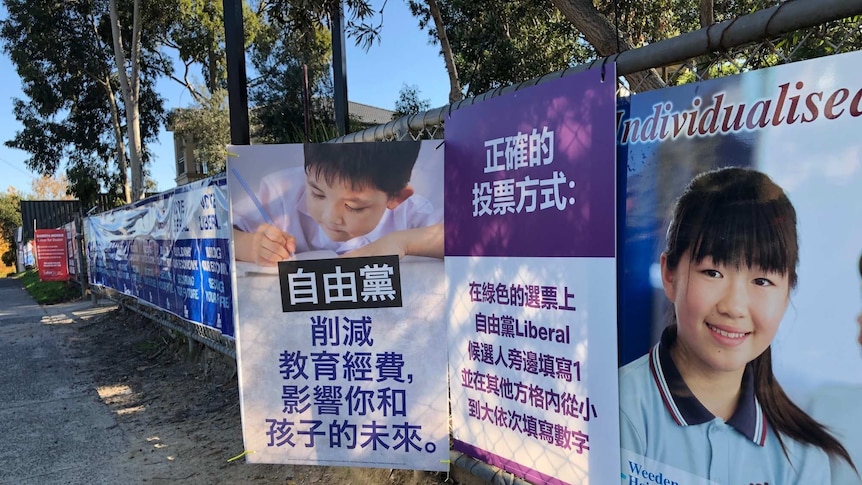 Two rival signs showing mandarin text on a chain fence, one depicts a Chinese child writing with pen and paper.