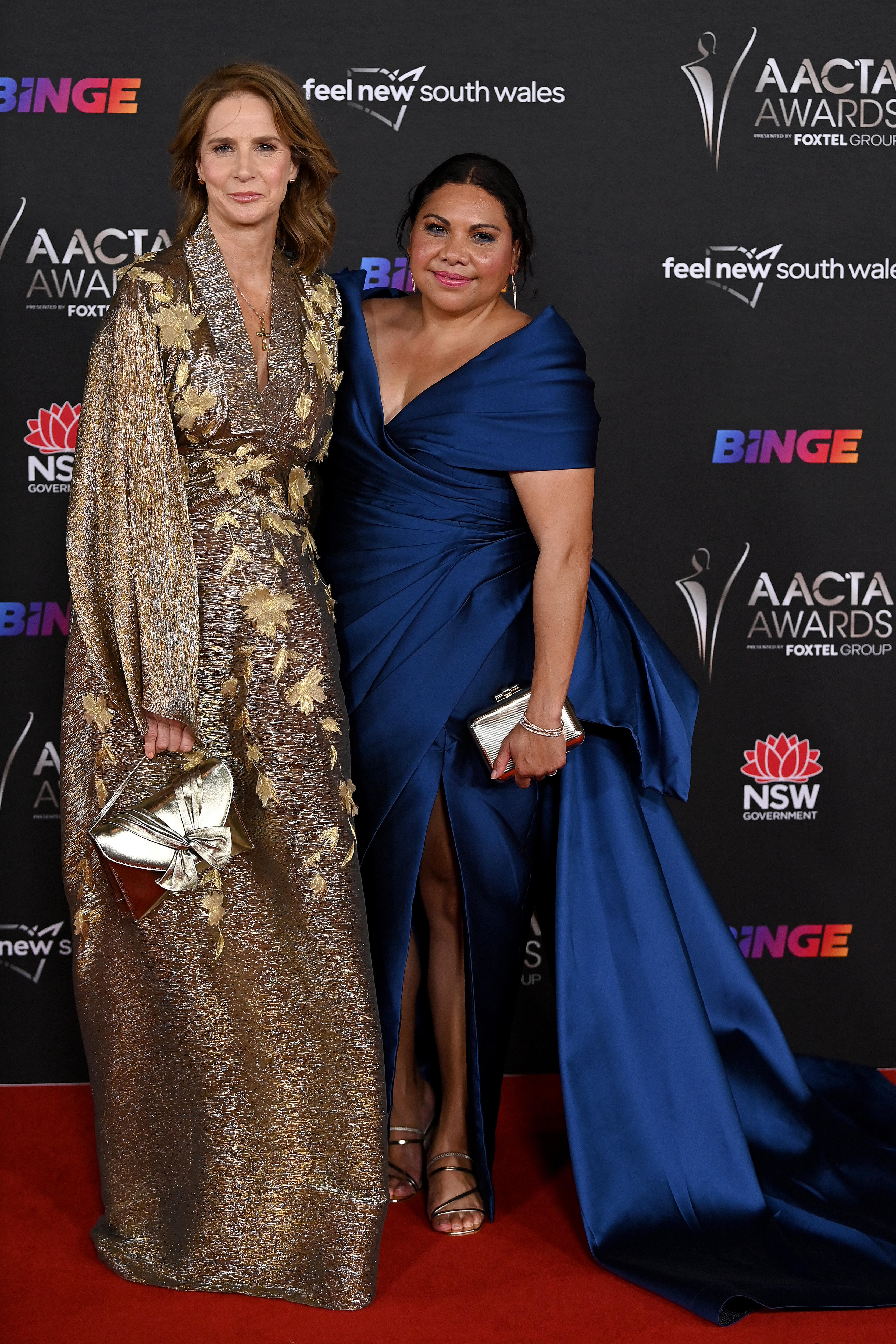 A woman in a gold and silver frock with a woman in a long blue ball gown at a red carpet event 