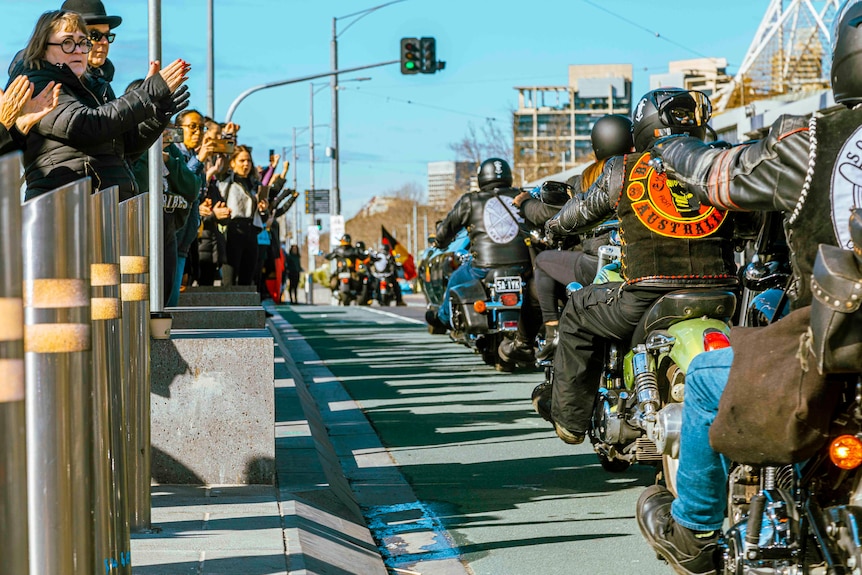 A line of motorcyle riders going across the bridge near Federation Square.