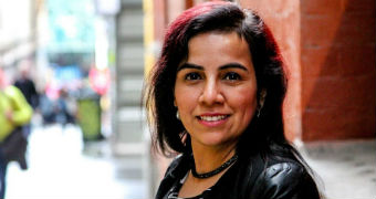 A woman in a black leather jacket smiles on a street in the daytime.