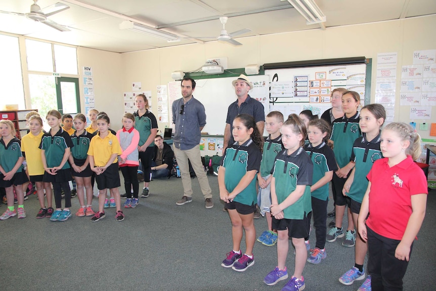 A classroom full of small kids with two adults standing in the middle singing