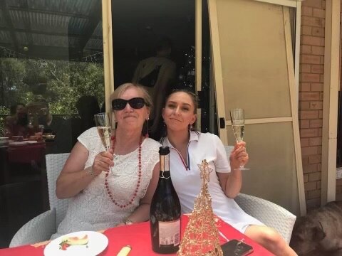 An older blonde lady and her young granddaughter cheers each other with champagne over Christmas lunch