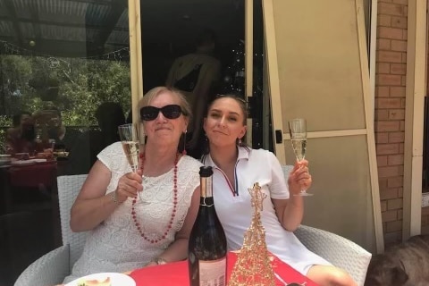 An older blonde lady and her young granddaughter cheers each other with champagne over Christmas lunch