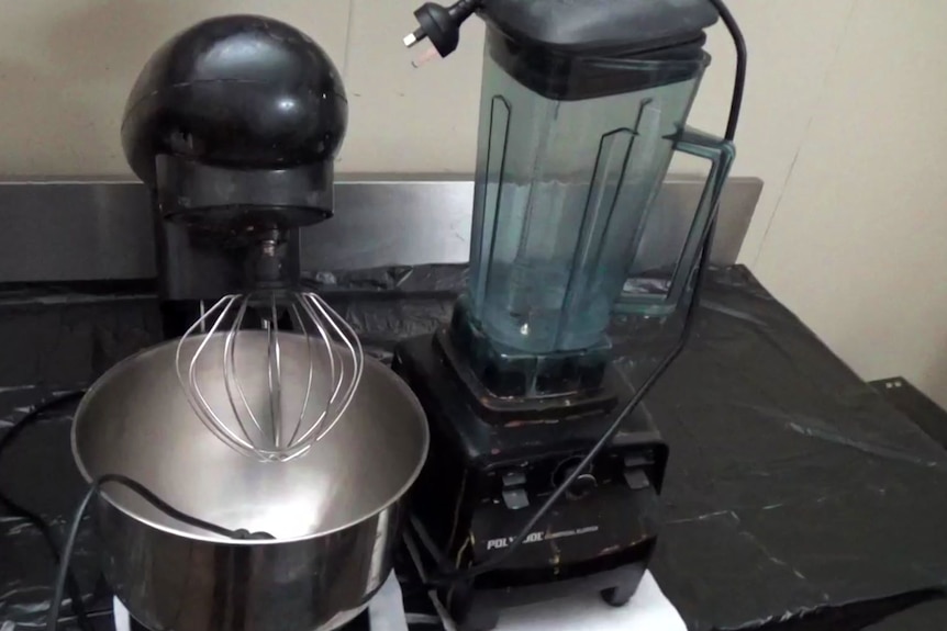 A household kitchen mixer and blender on a bench covered in black plastic.