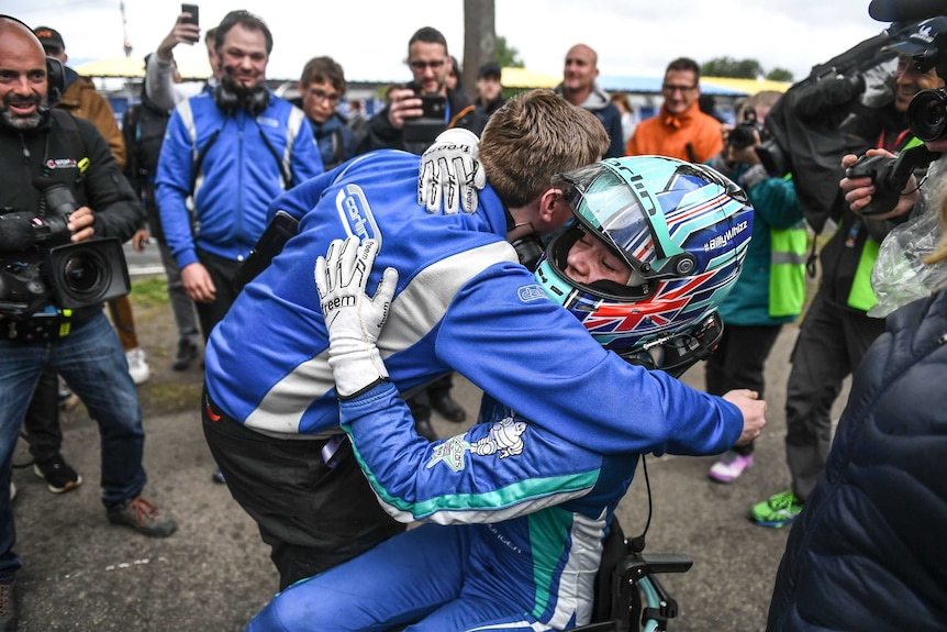 Billy Monger hugs a supporter in his wheelchair, wearing full racing kit