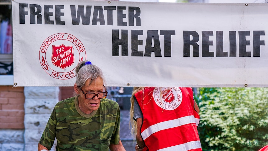 An elderly lady holds a bottle of water in front of a Salvation Army free water station in Phoenix