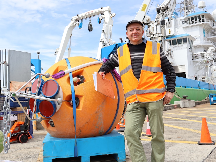 Dr Benoit Legresy stands next to a research flotation device on a ship.