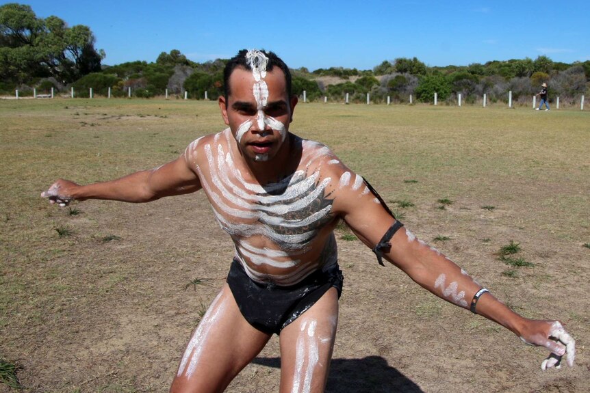 An indigenous man wearing white body paint dancing in a park.