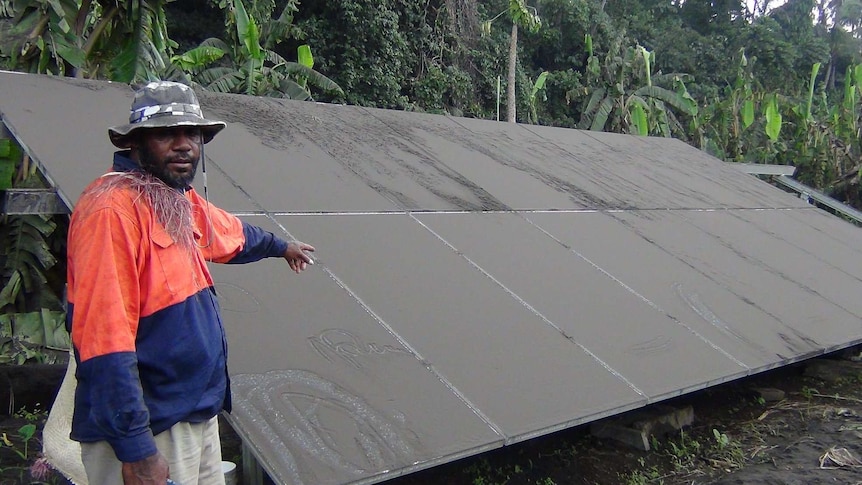 A man stands beside what appears to be a solar panel covered in ash.