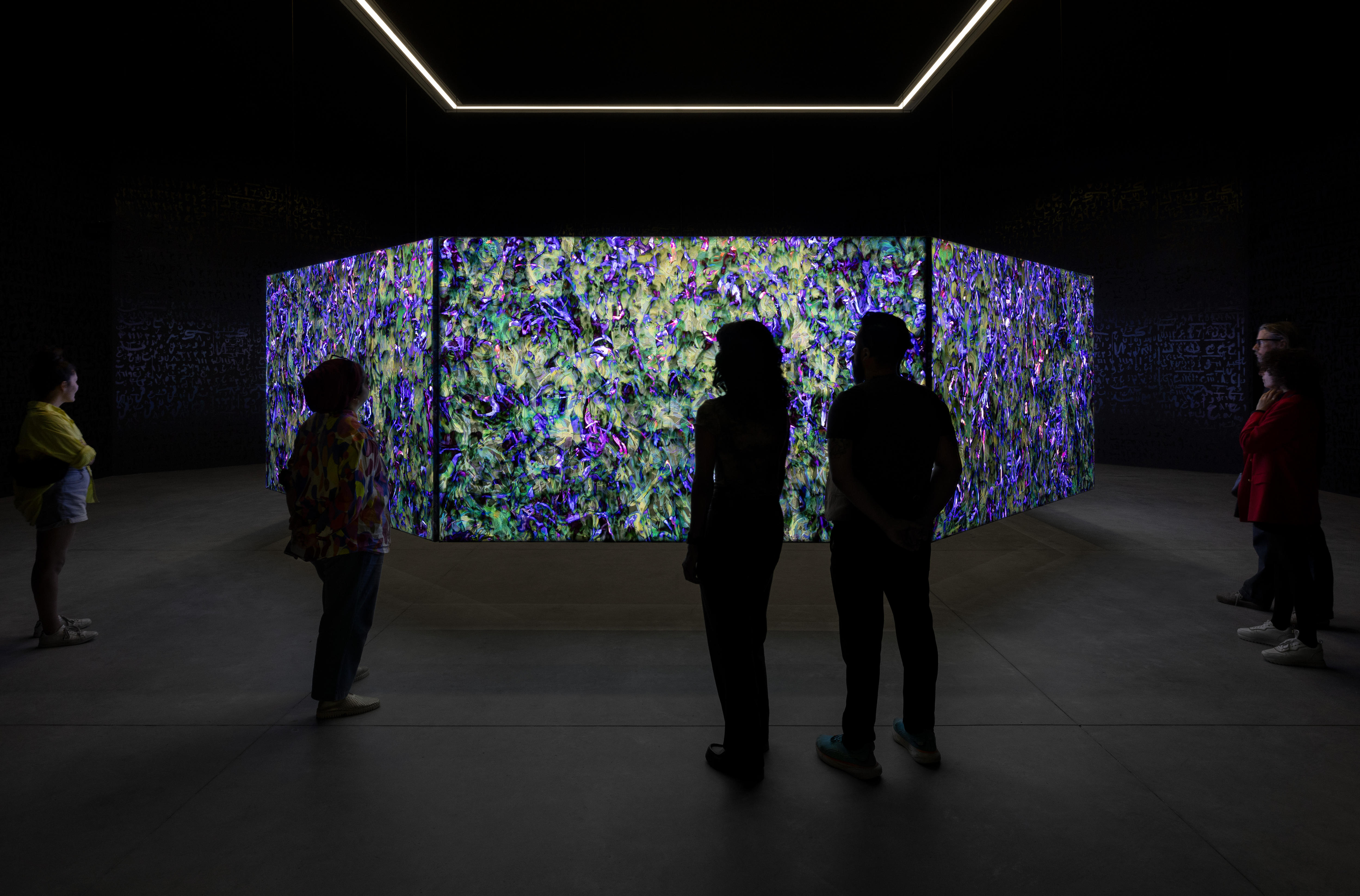 A group of people look at a series of screens hung in the air. The screens show intricate purple and blue patterns pulsating.